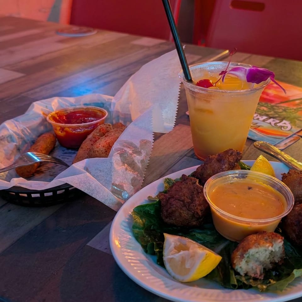 Restaurant table with fried meatballs, dipping sauce, lemon, bread, and a garnished tropical drink.