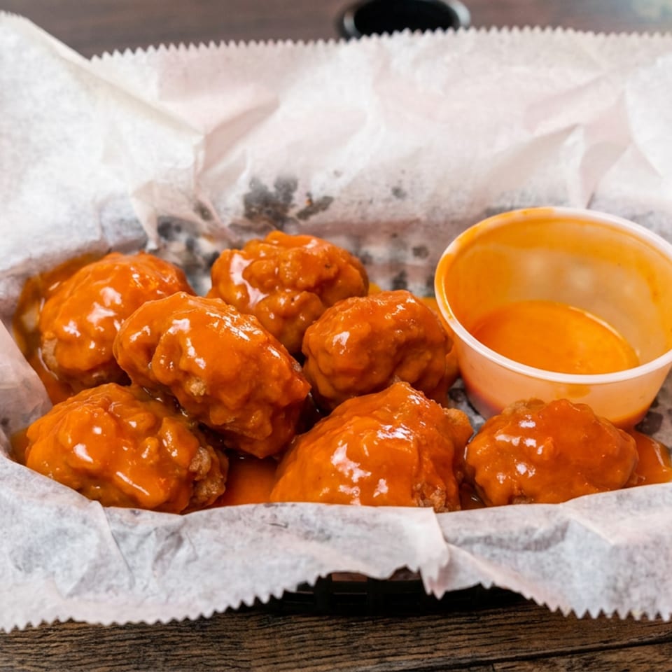 Basket of glazed orange chicken wings with dipping sauce on parchment paper atop a rustic wooden table.